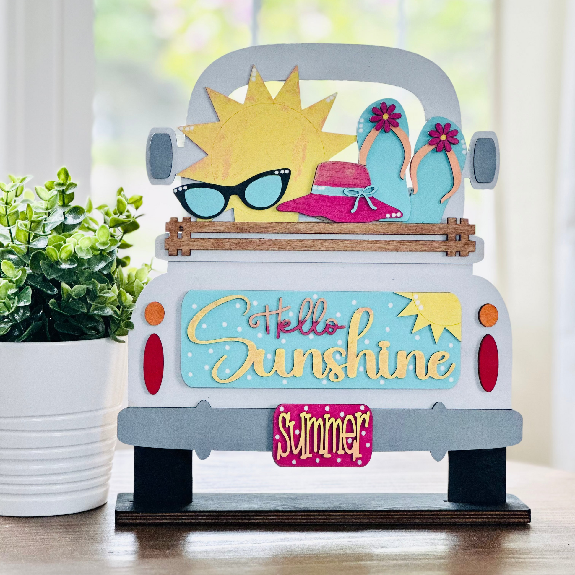 A decorative wood insert featuring a colorful illustration of a sun wearing sunglasses and a hat, with text that reads 'Hello Sunshine' and 'Summer'. The piece is designed to be interchangeable and is part of a seasonal home decor set.