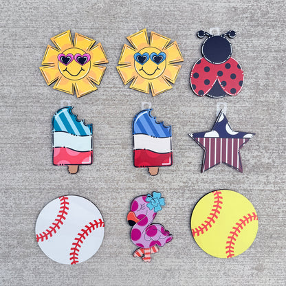  patriotic summer and sports themes, including two smiling yellow suns with sunglasses, a ladybug, two popsicles with a French tricolor design, a star, a baseball, a flamingo, and a yellow softball.