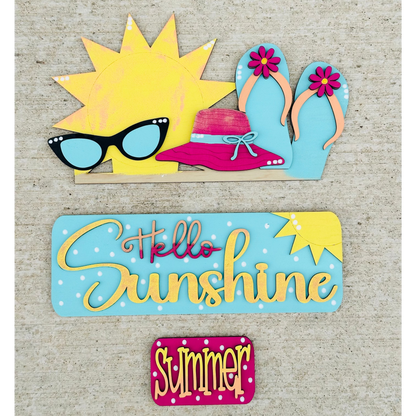 A decorative wood insert featuring a colorful illustration of a sun wearing sunglasses and a hat, with text that reads 'Hello Sunshine' and 'Summer'. The piece is designed to be interchangeable and is part of a seasonal home decor set.