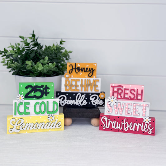 Set of colorful wooden signs with text on a white surface with a plant in the background