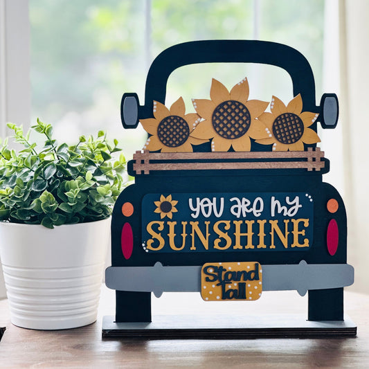 Decorative sign shaped like a truck with sunflowers and 'You are my sunshine' text on a wooden surface.