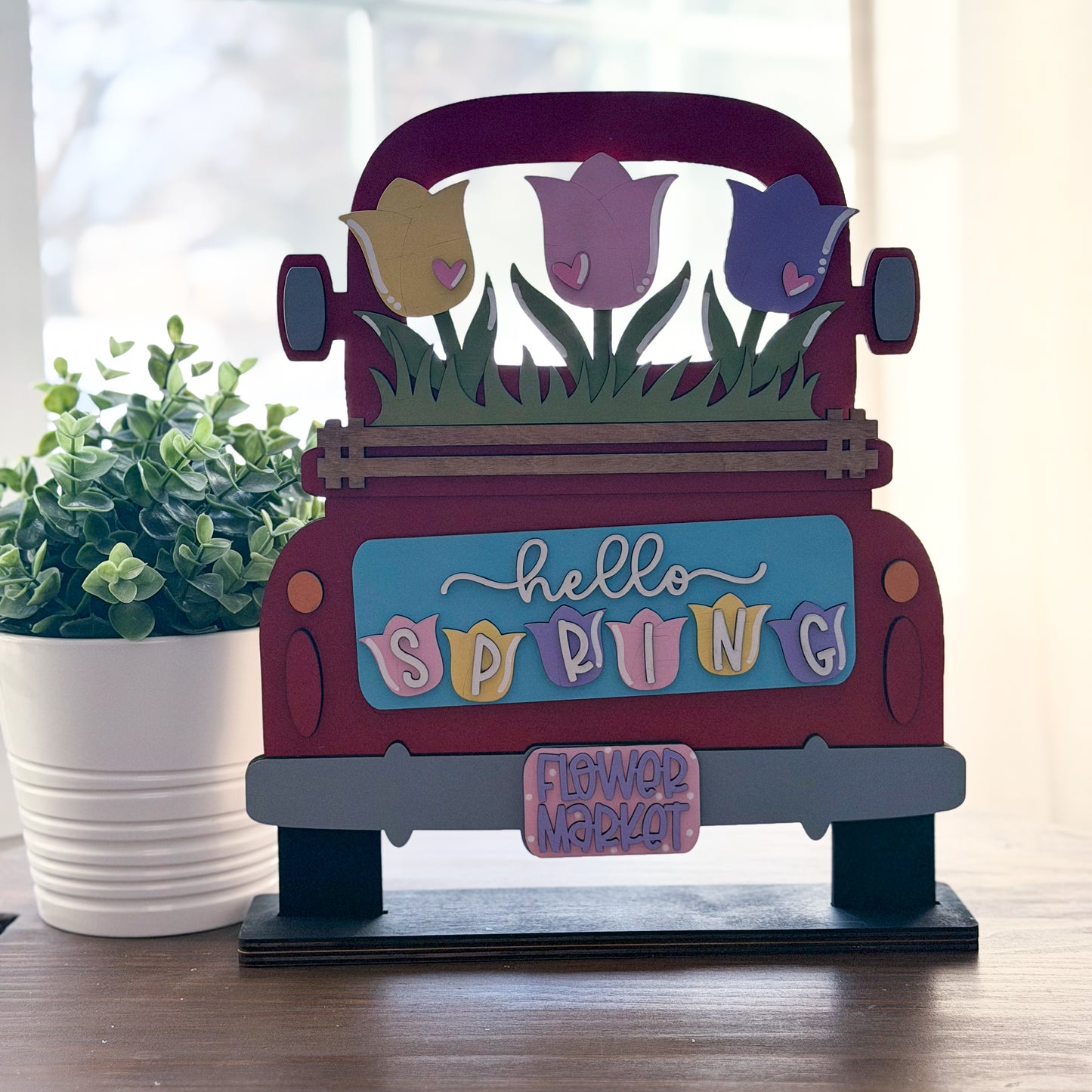 Decorative sign shaped like a red truck with spring-themed elements on a wooden surface.