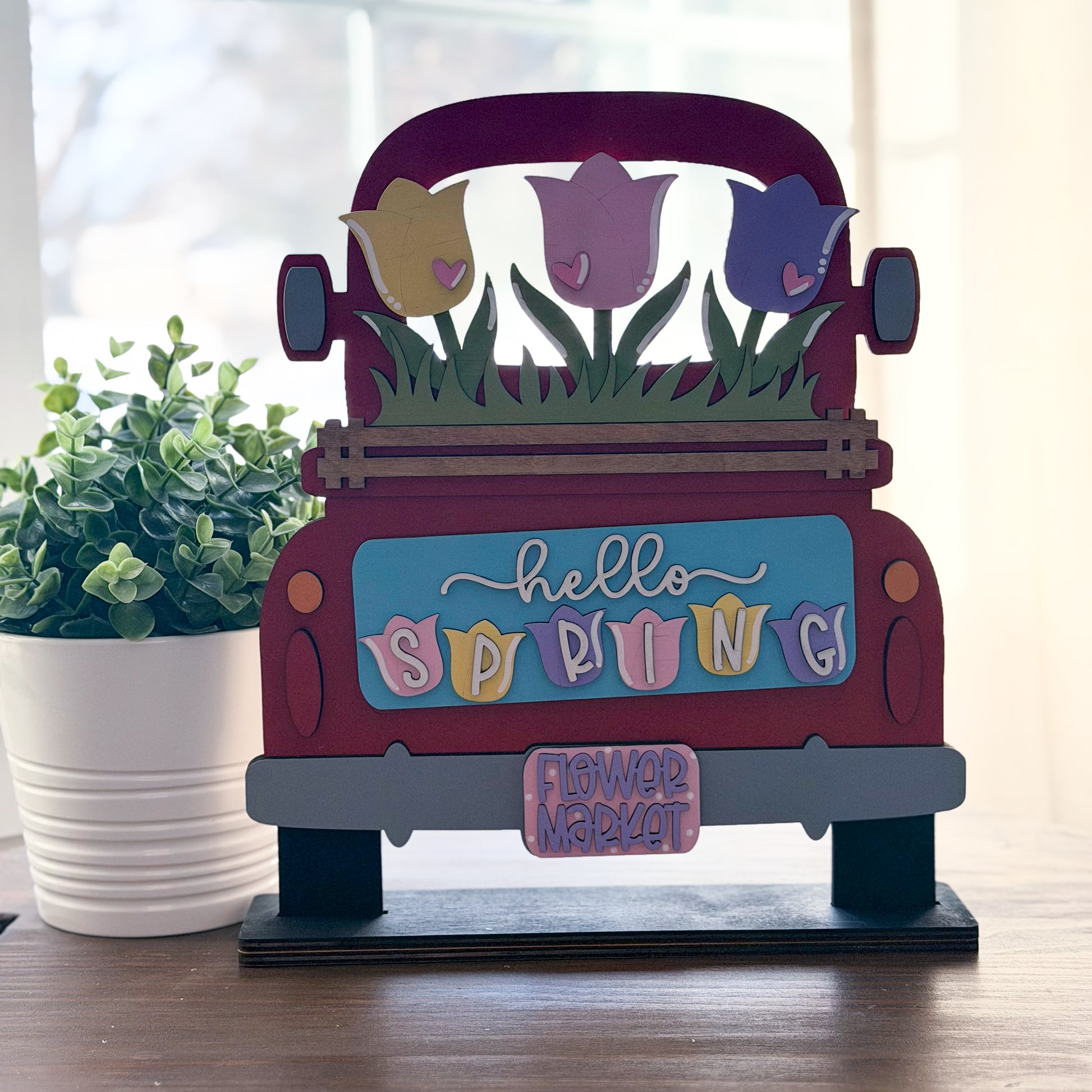 Decorative sign shaped like a red truck with spring-themed elements on a wooden surface.