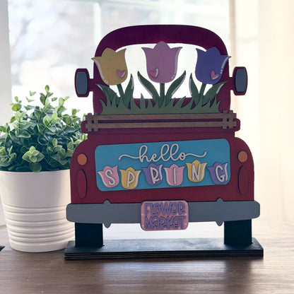 Decorative sign shaped like a red truck with spring-themed elements on a wooden surface.