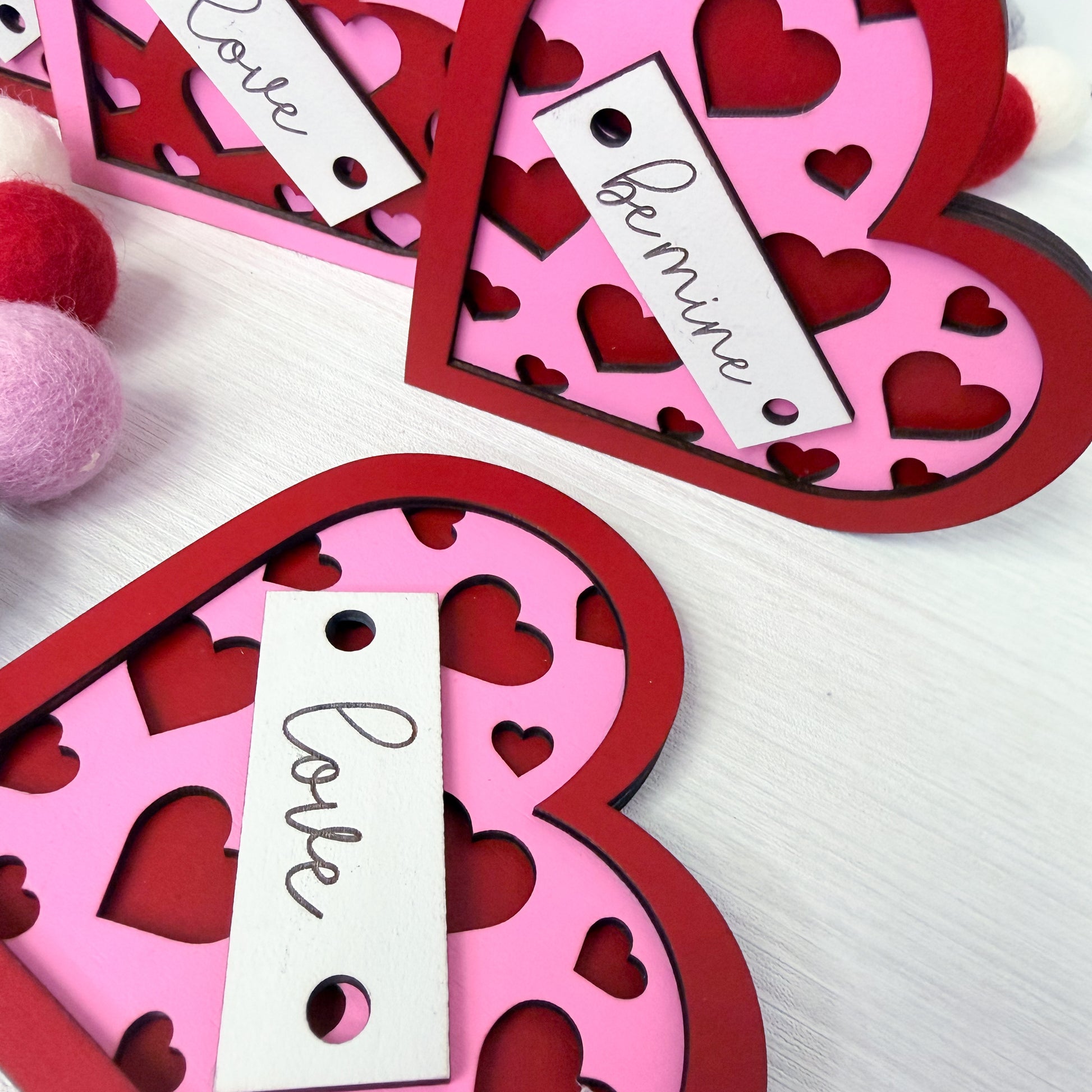Heart-shaped pink and red cutout decorations with 'Love' and 'Be mine' tags on a white background.