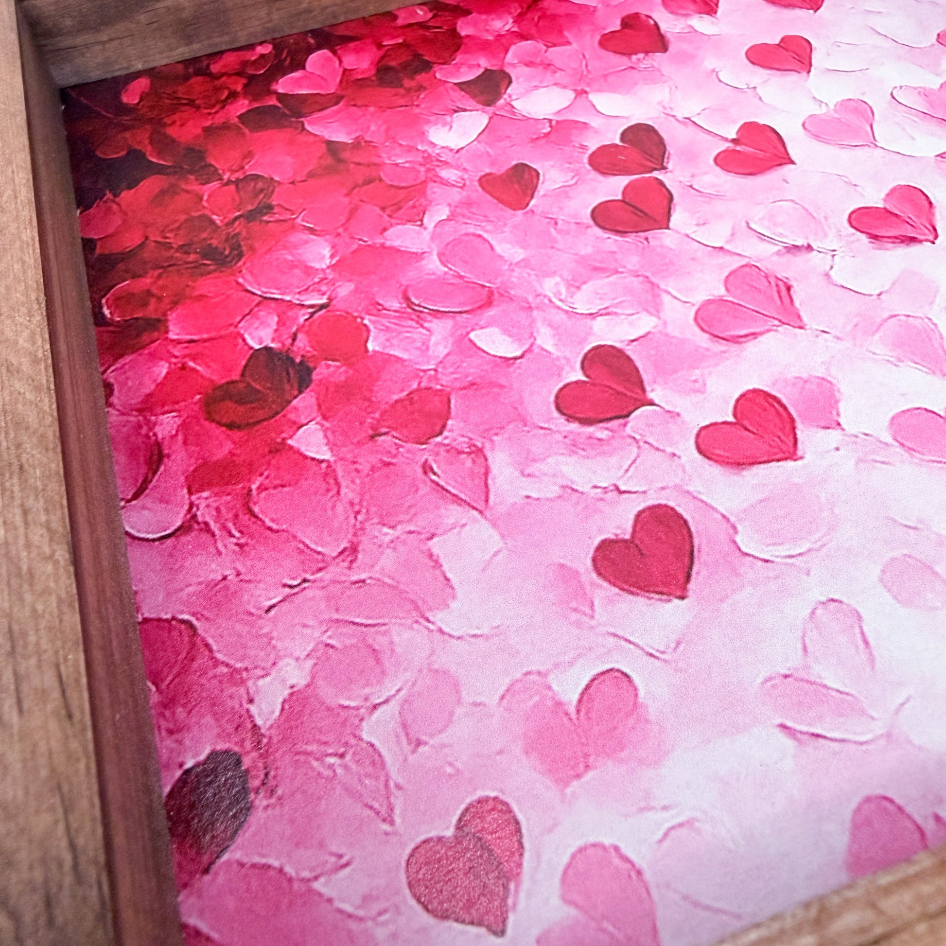 Pink and red heart-shaped confetti on a pink background with a wooden frame.