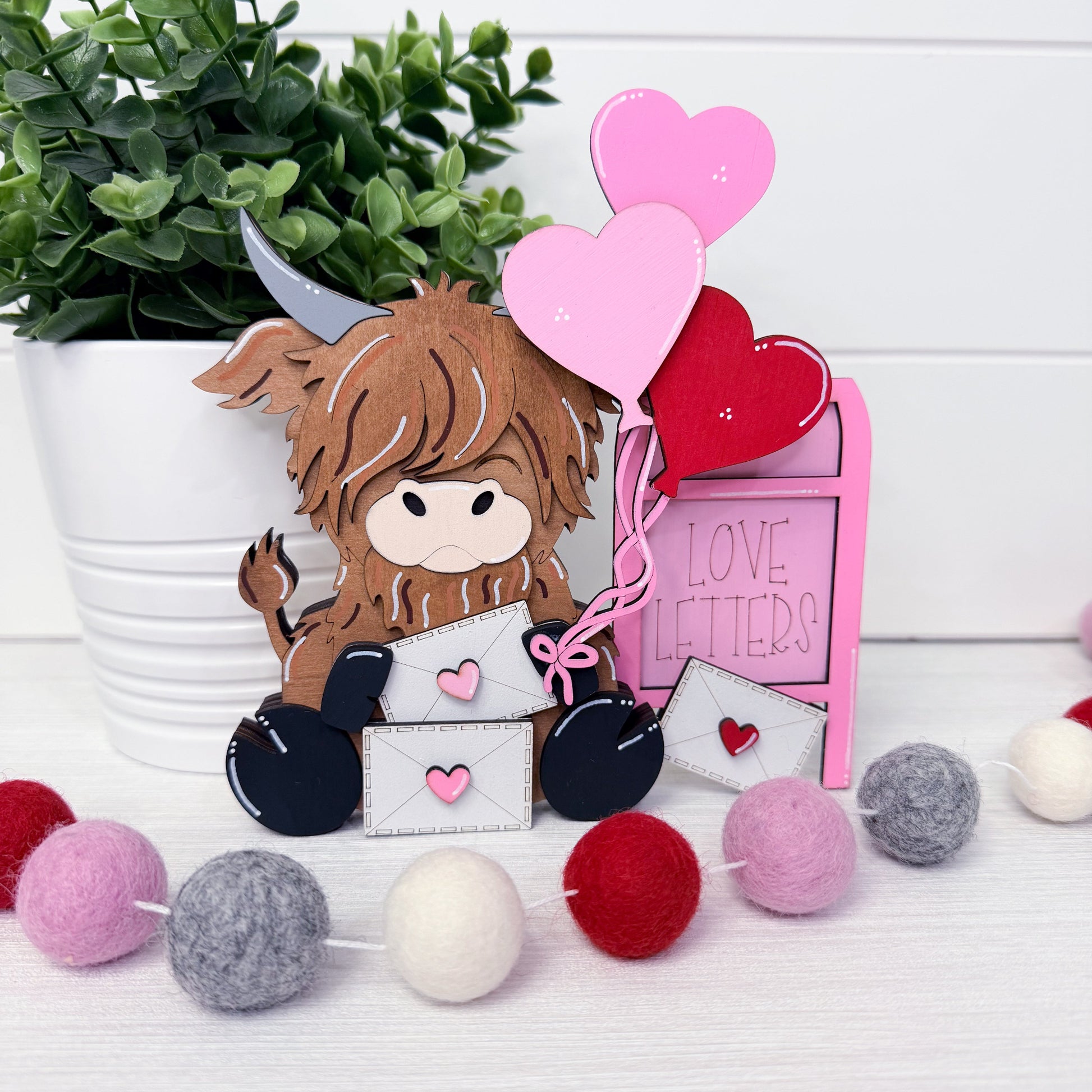 Valentine's Day-themed decor with a cow character, heart balloons, and decorative balls on a white surface.
