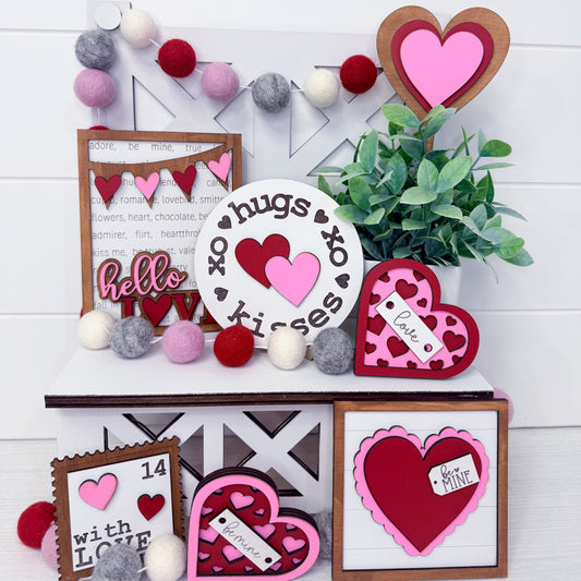 Valentine's Day-themed decor with heart-shaped signs and a plant on a white wooden background.
