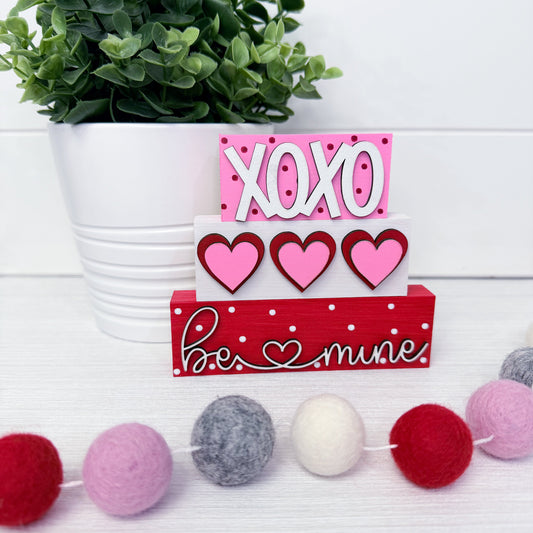 Decorative sign with 'XOXO' and hearts next to a plant and pom-pom garland.