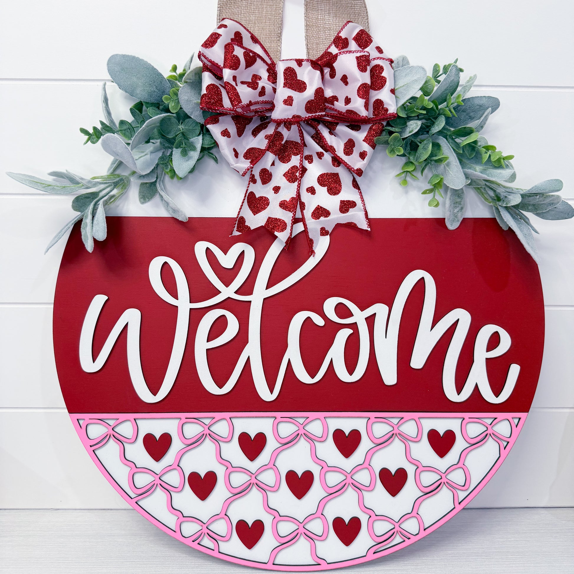 Decorative door hanger with 'Welcome' text, heart patterns, and a bow on a white background