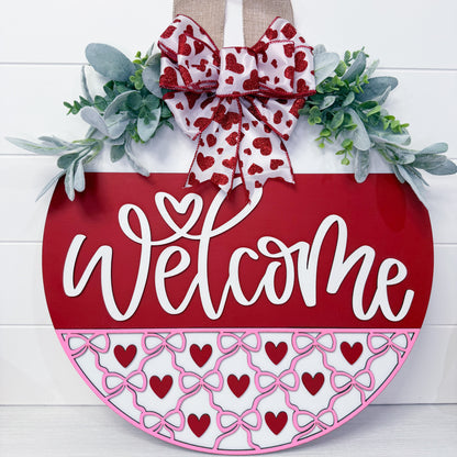 Decorative door hanger with 'Welcome' text, heart patterns, and a bow on a white background