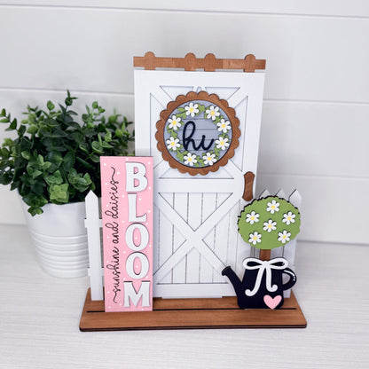 Decorative items including a pink 'BLOOM' sign, white board with wooden frame, and small plant on a white surface.