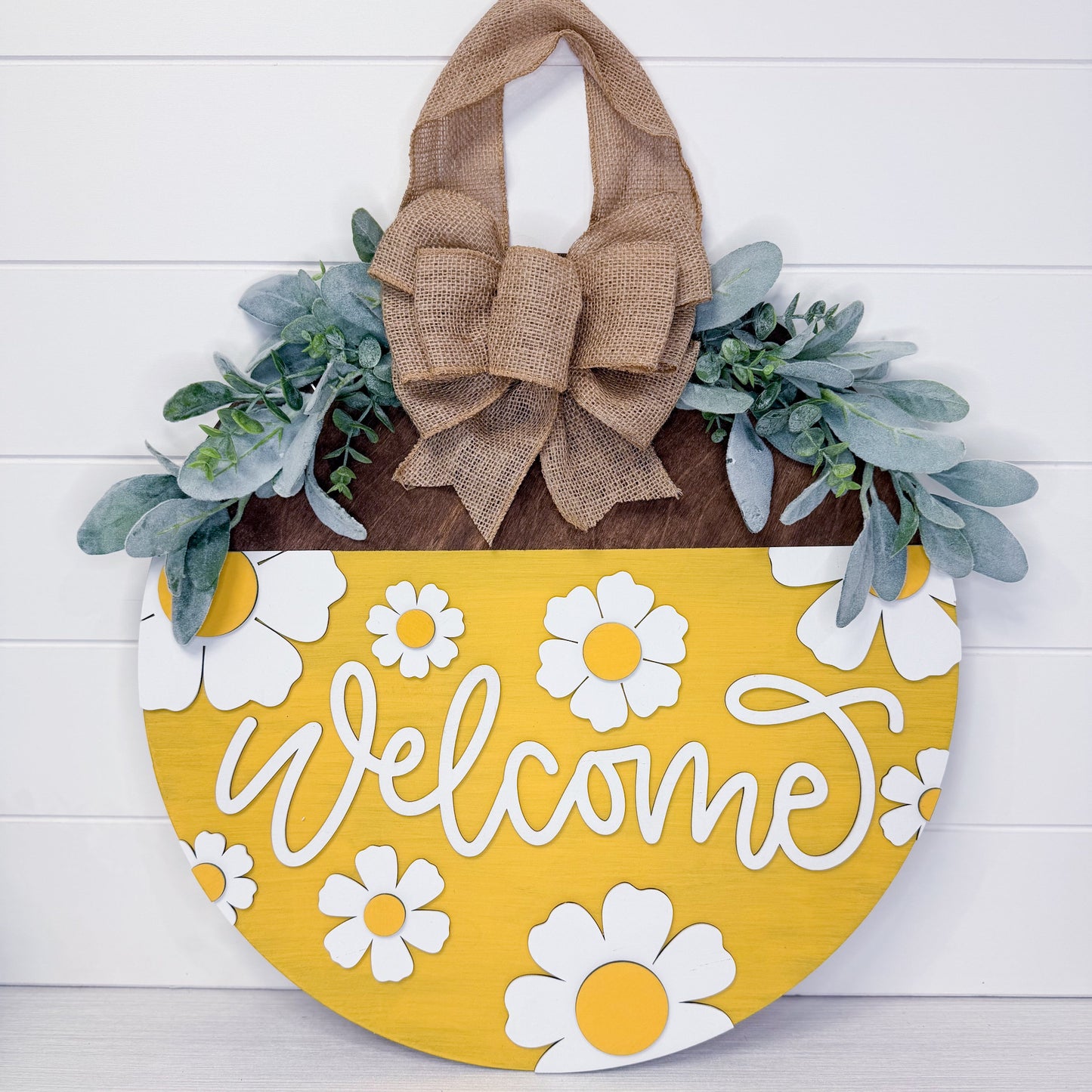 Decorative door hanger with 'Welcome' text, flowers, and a burlap bow on a white background