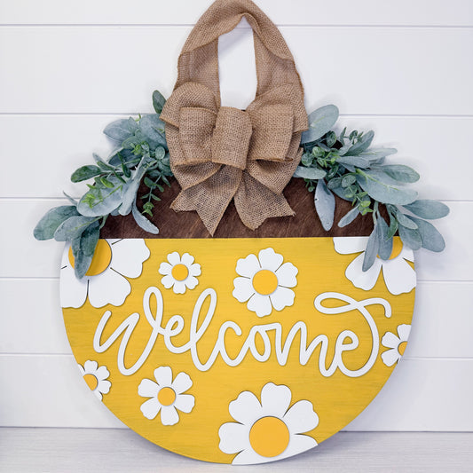 Decorative door hanger with 'Welcome' text, flowers, and a burlap bow on a white background