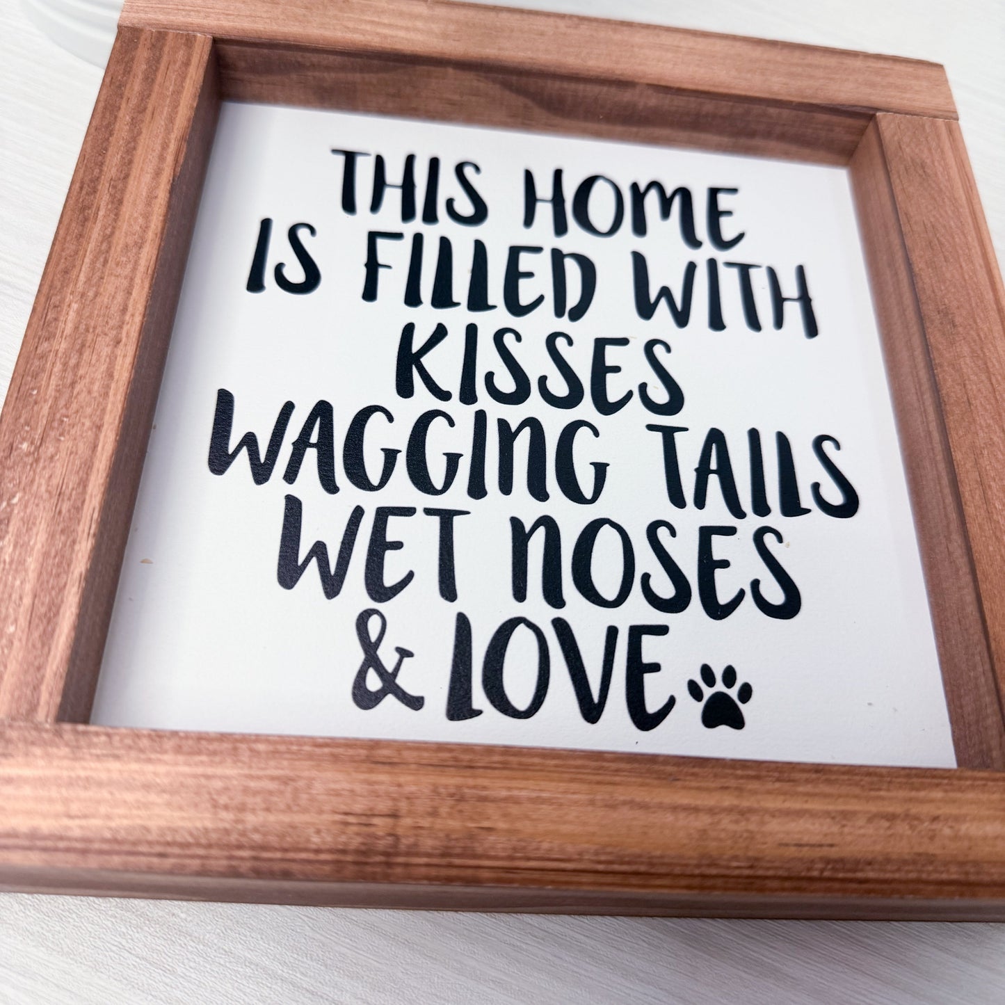 Framed sign with text 'This home is filled with kisses, wagging tails, wet noses & love' on a white background.