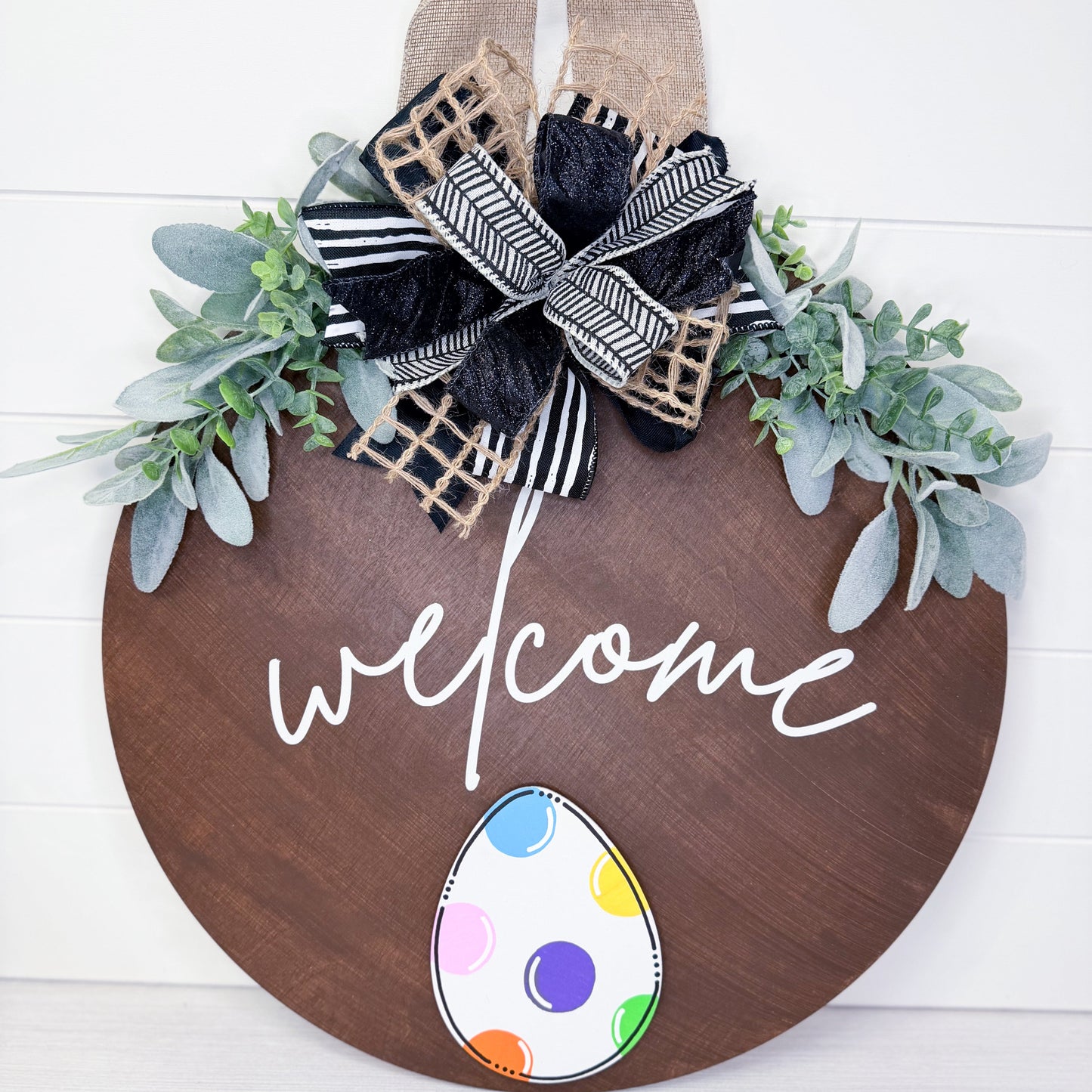 Wooden door hanger with 'welcome' text, decorative bow, and Easter egg design on a white background.