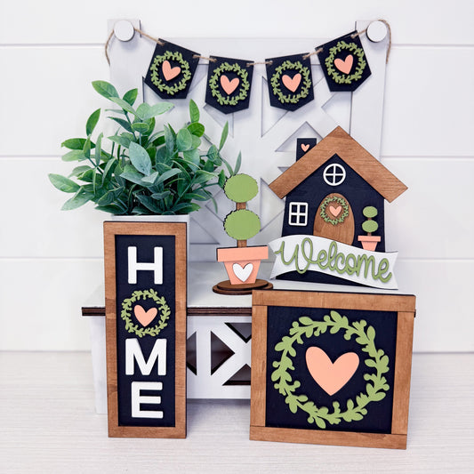 Decorative home signs with plants and heart designs on a white wooden background