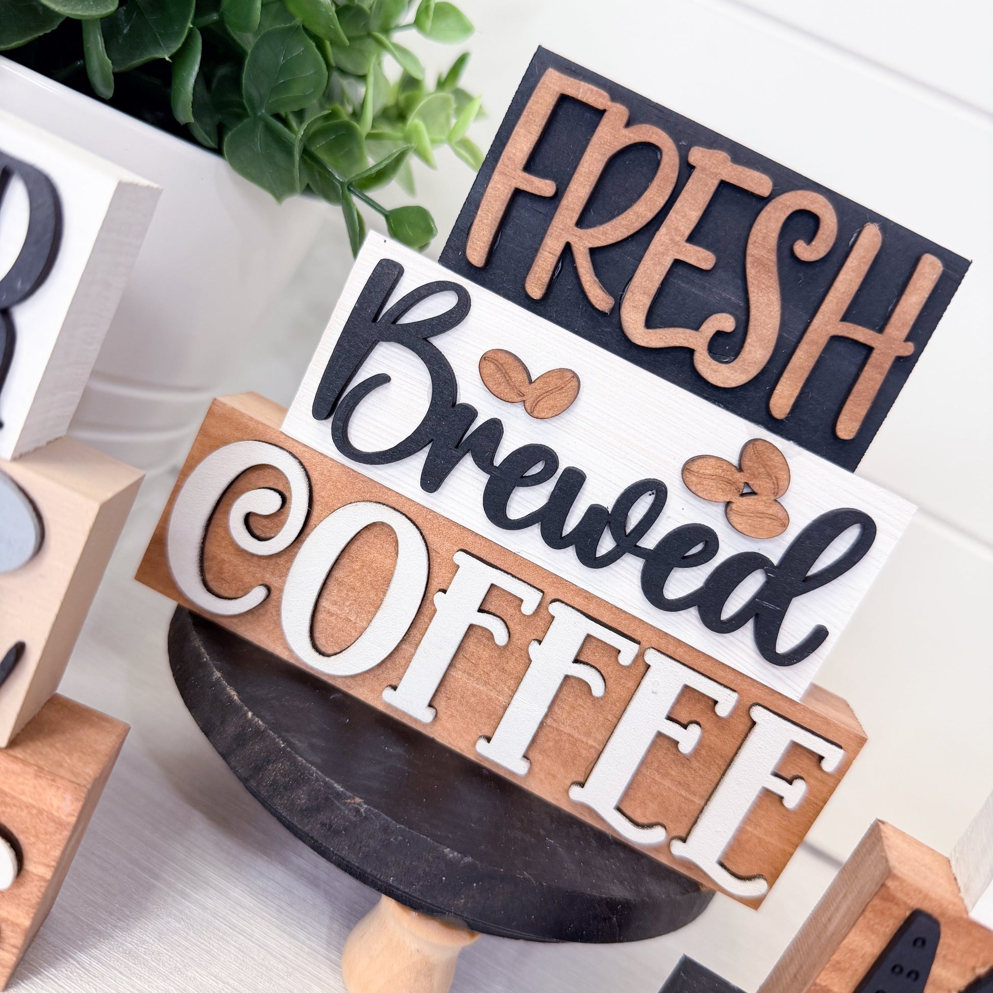 Wooden sign with 'Fresh Brewed Coffee' text on a white surface with greenery.
