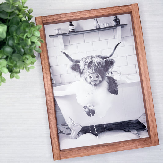 Framed black and white photo of a cow in a bathtub on a tiled wall.