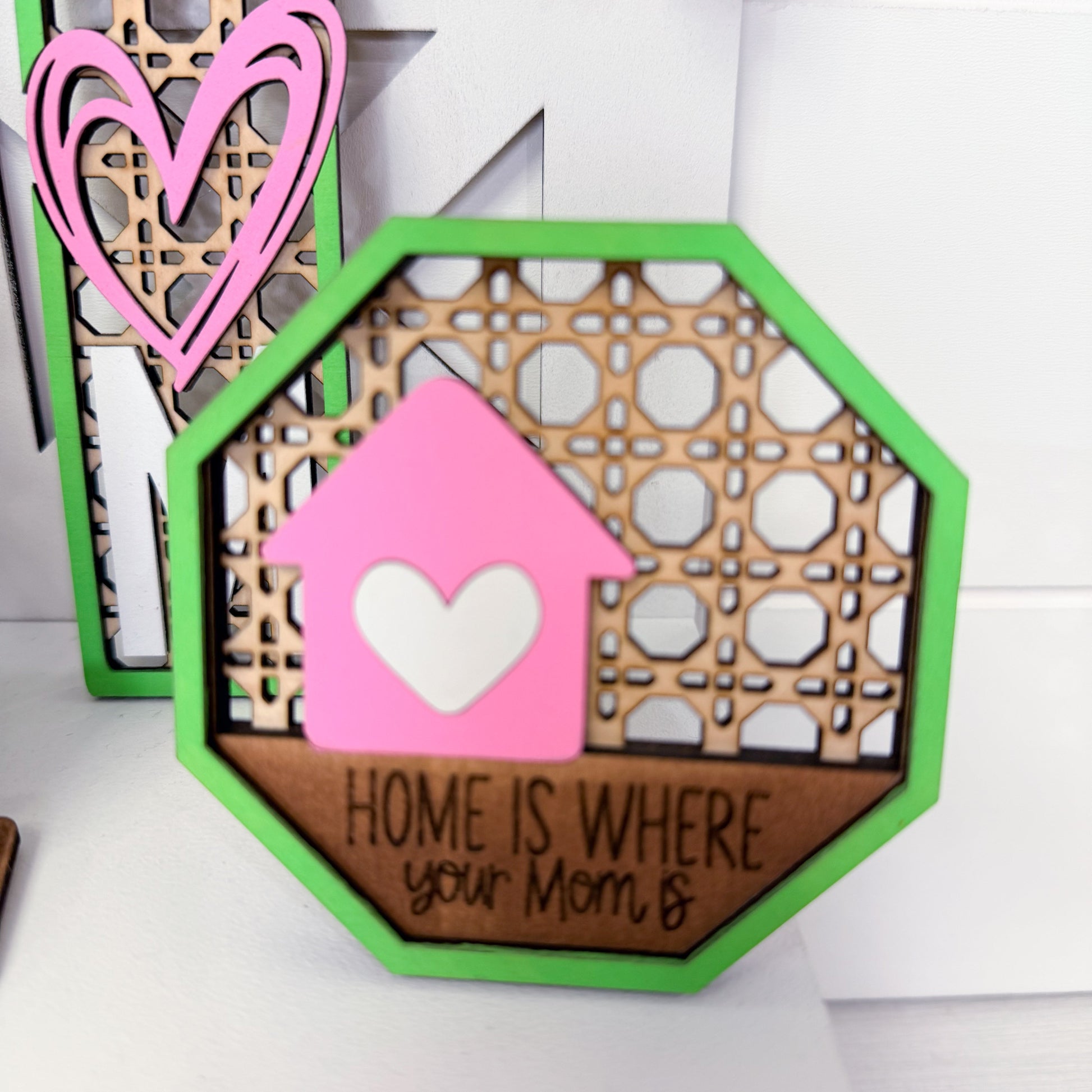 Decorative wooden sign with pink heart and text 'Home is where your mom is' on a white background