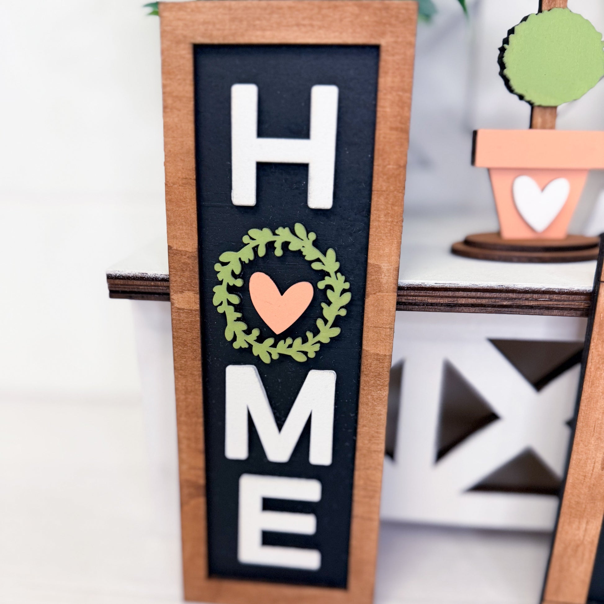 Decorative sign with 'HOME' and heart wreath design on a black background