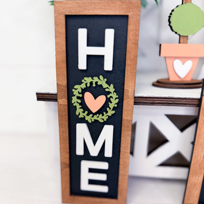 Decorative sign with 'HOME' and heart wreath design on a black background