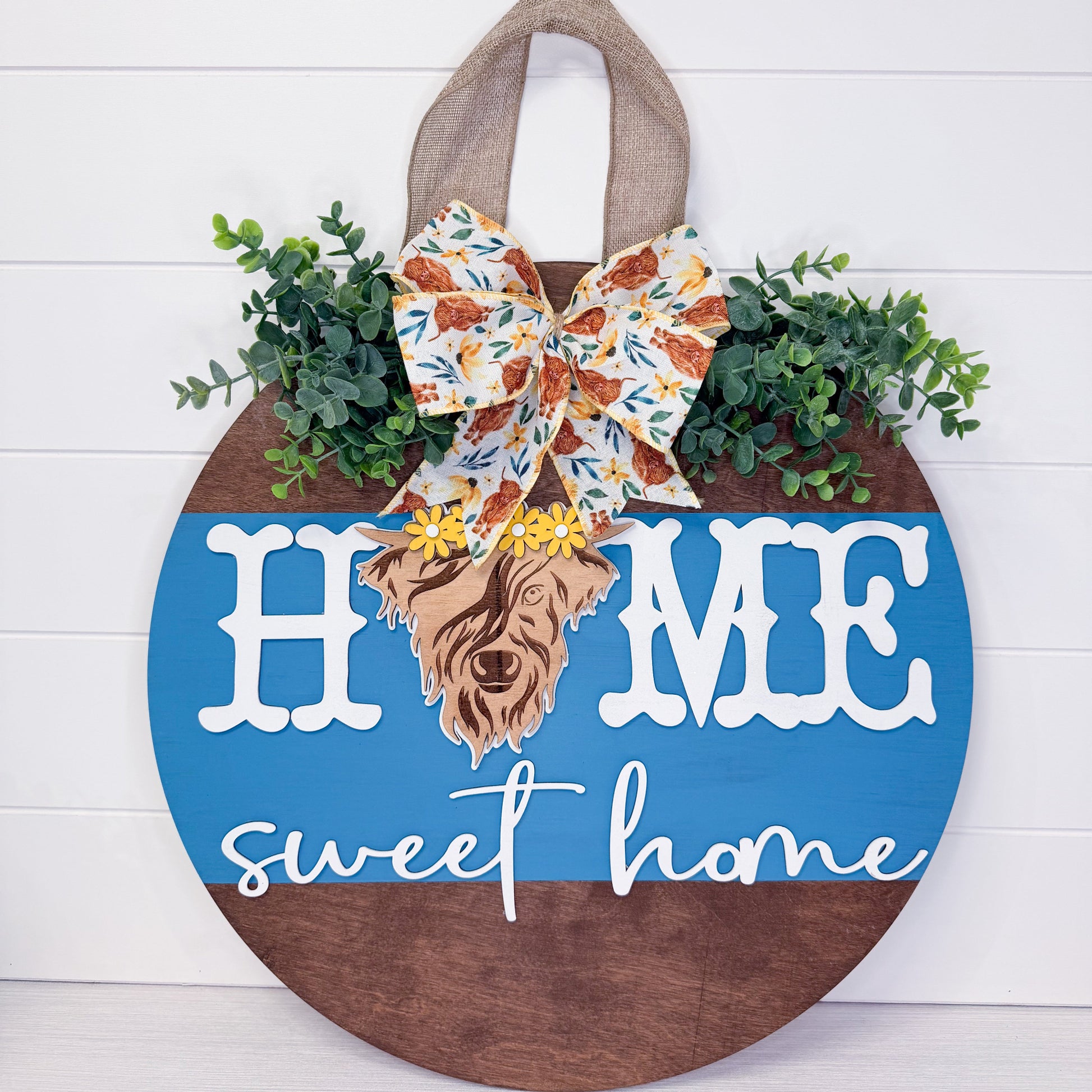 Decorative sign with 'Home sweet home' text, plants, and a bow on a white background
