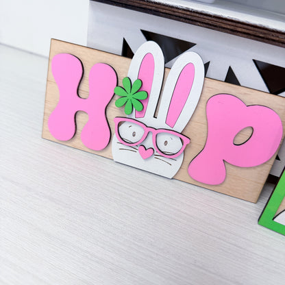 Wooden sign with pink letters 'HOP' and a bunny face on a white surface.