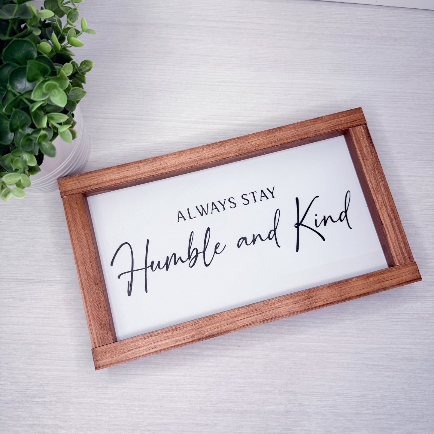 Wooden-framed sign with 'Always Stay Humble and Kind' text on a light background