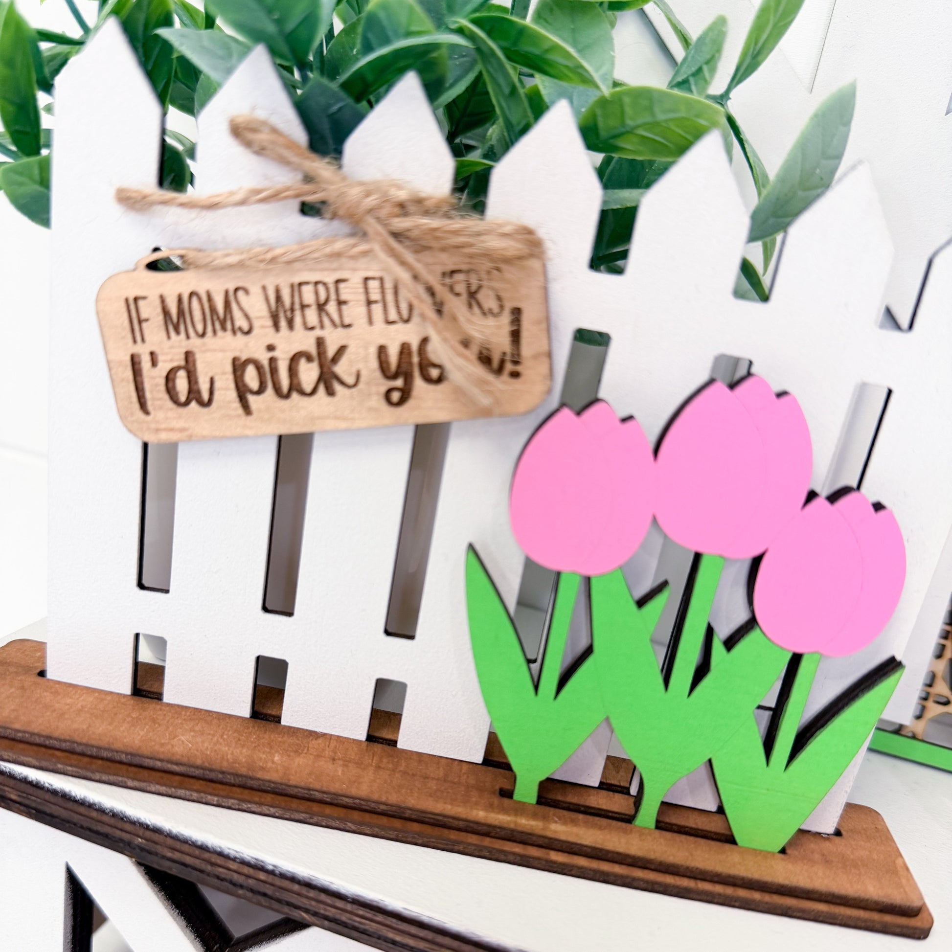 Decorative sign with pink tulips and a wooden picket fence, featuring a humorous message.