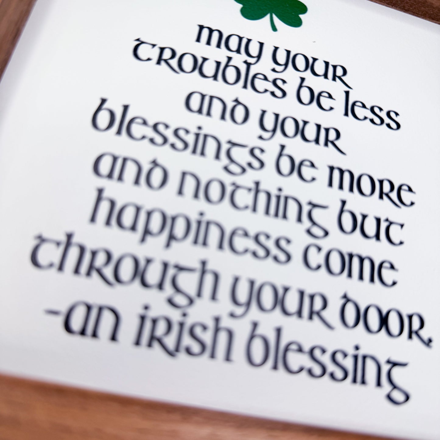 Irish blessing text on a white card with a green clover symbol, placed on a wooden surface.