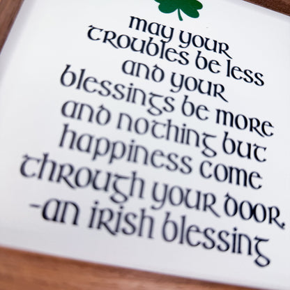 Irish blessing text on a white card with a green clover symbol, placed on a wooden surface.