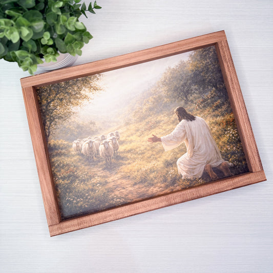 Framed artwork of a religious scene with a shepherd and sheep on a wooden sign.