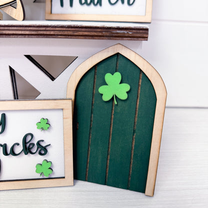 Green fairy door with wooden frame and shamrock decorations on a white surface.