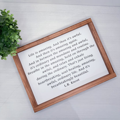 Wooden-framed print with a quote by L.R. Knost on a light background with a plant.