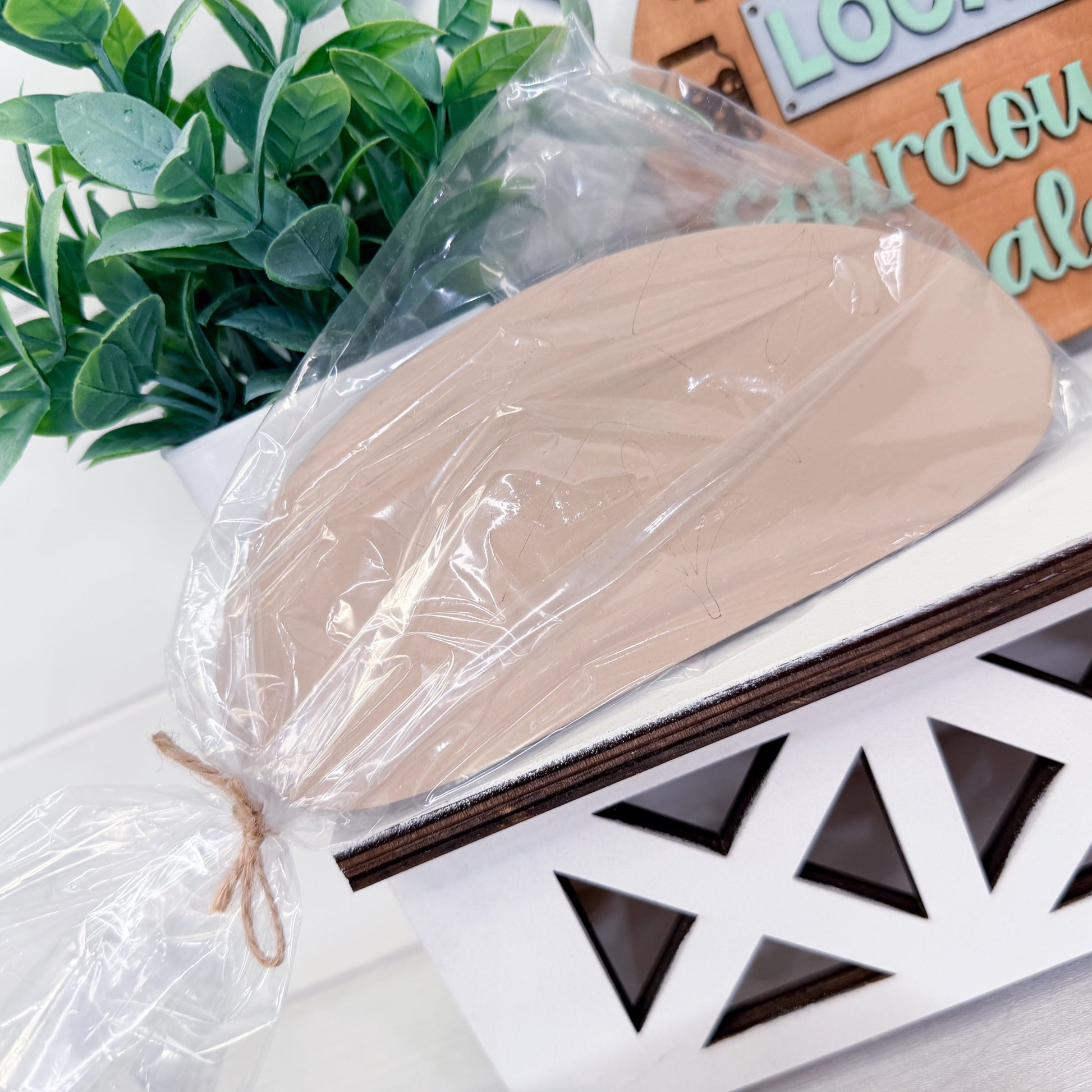 Wooden loaf in clear plastic wrap on a decorative surface with plants in the background