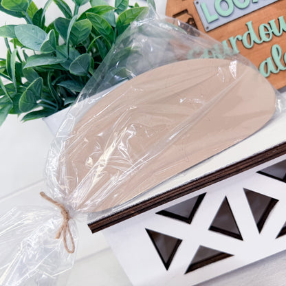 Wooden loaf in clear plastic wrap on a decorative surface with plants in the background