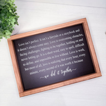 Wooden-framed plaque with a romantic quote on a white surface with a plant in the corner.