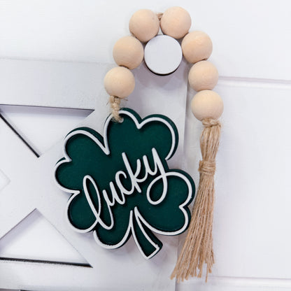 Decorative wall hanging with wooden beads and a shamrock-shaped sign saying 'lucky' on a white background.