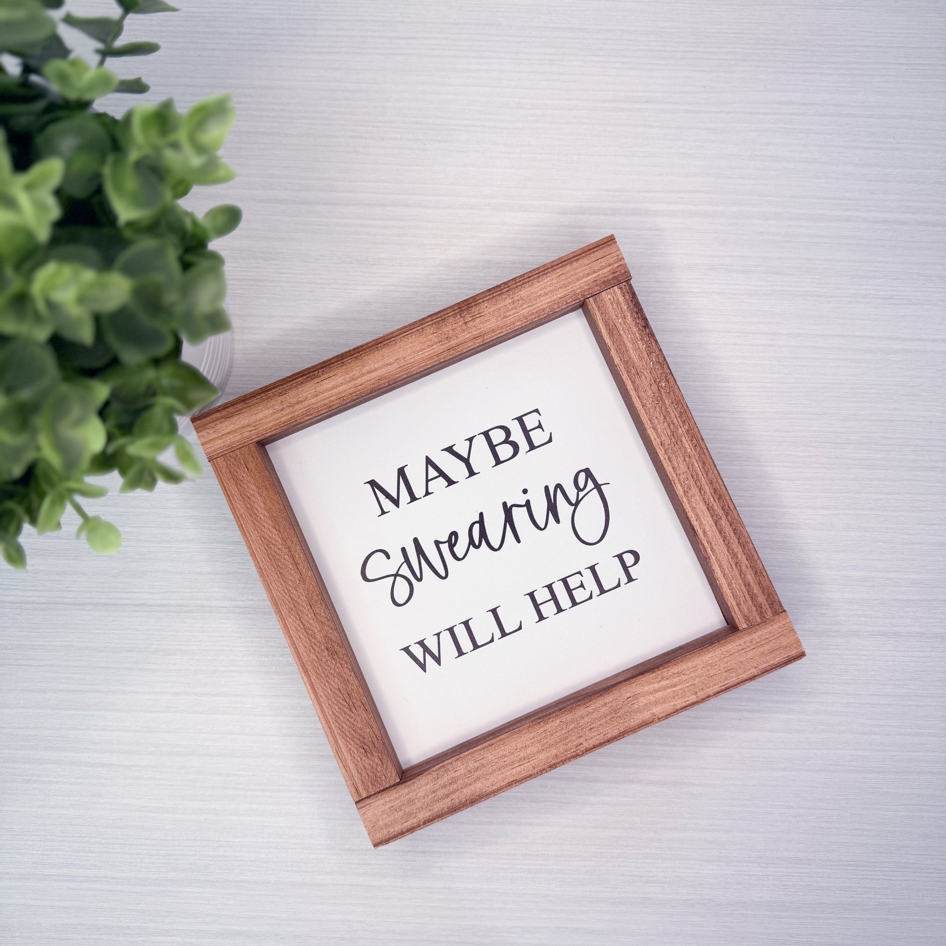 Wooden-framed sign with text 'Maybe Swearing Will Help' on a light background