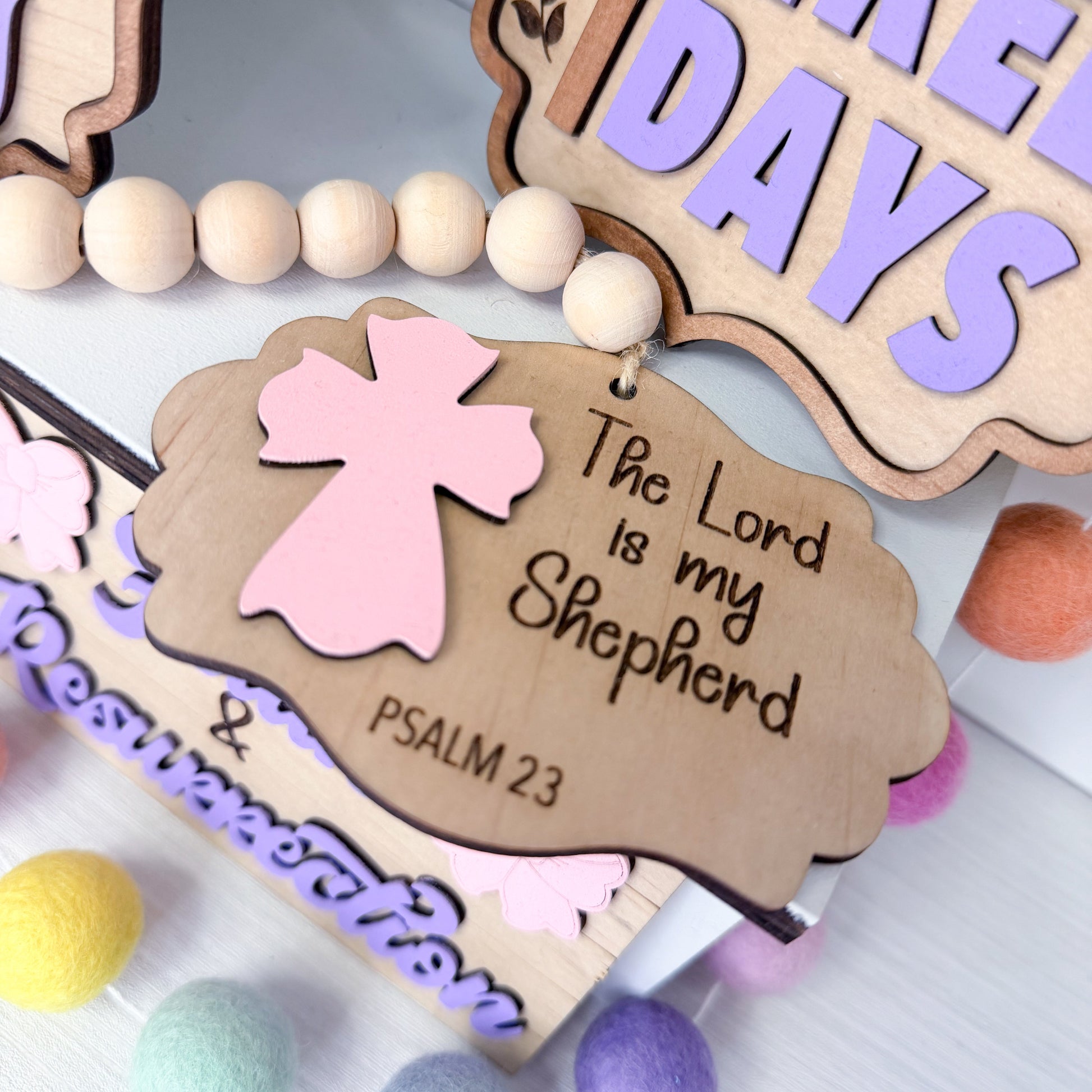 Decorative wooden tag with pink angel and 'The Lord is my Shepherd' text, surrounded by colorful beads.