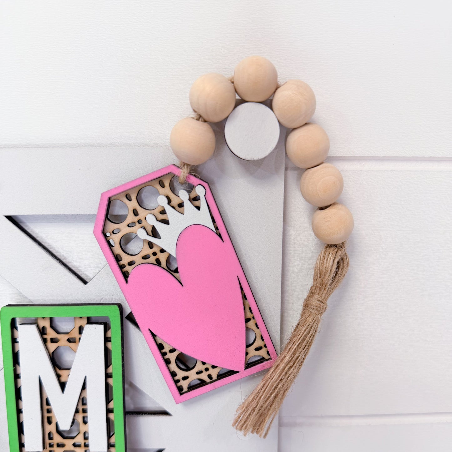 Decorative tag with pink heart design, wooden beads, and tassel on a white background