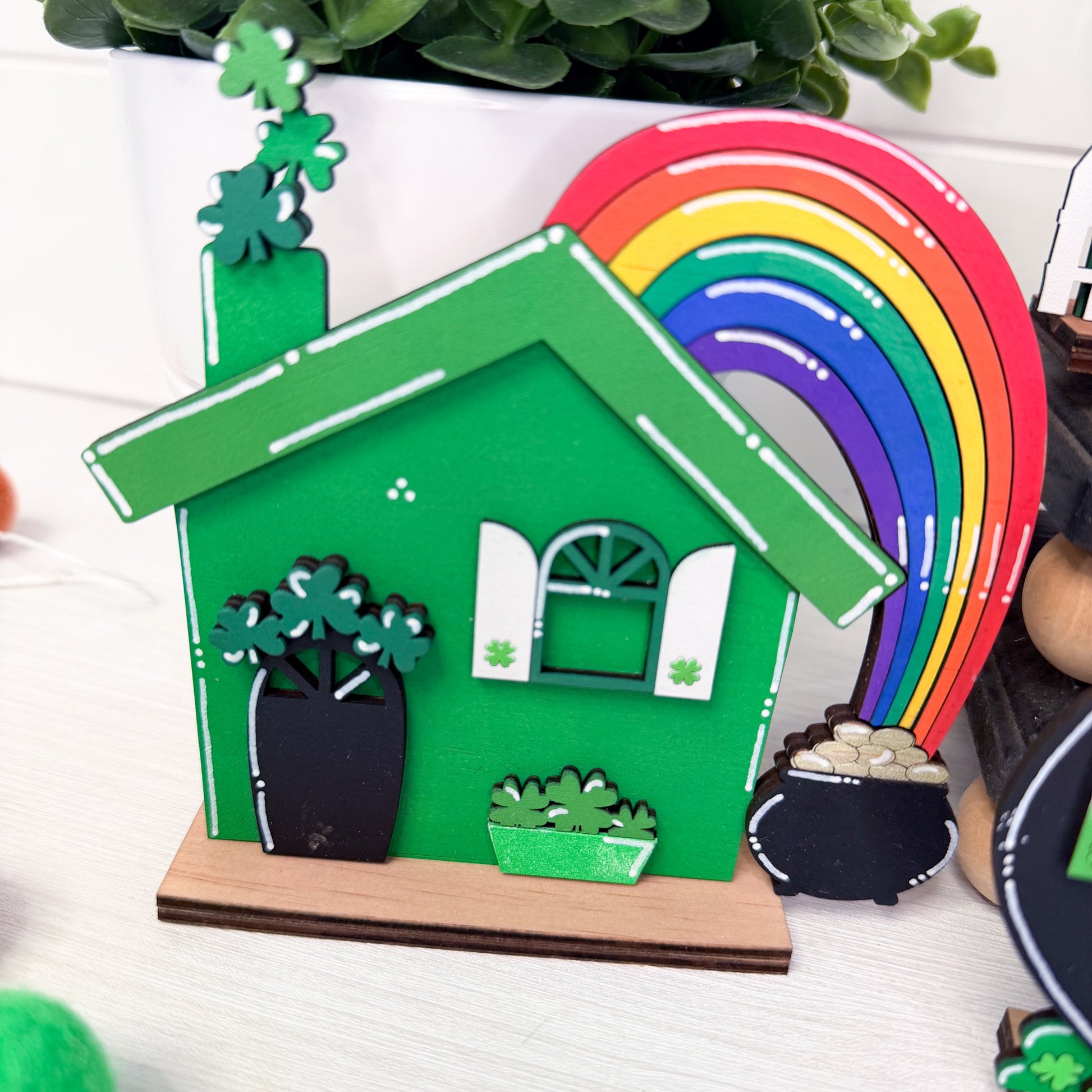 Green house-shaped piece with rainbow, pot of gold, and shamrocks on a white background