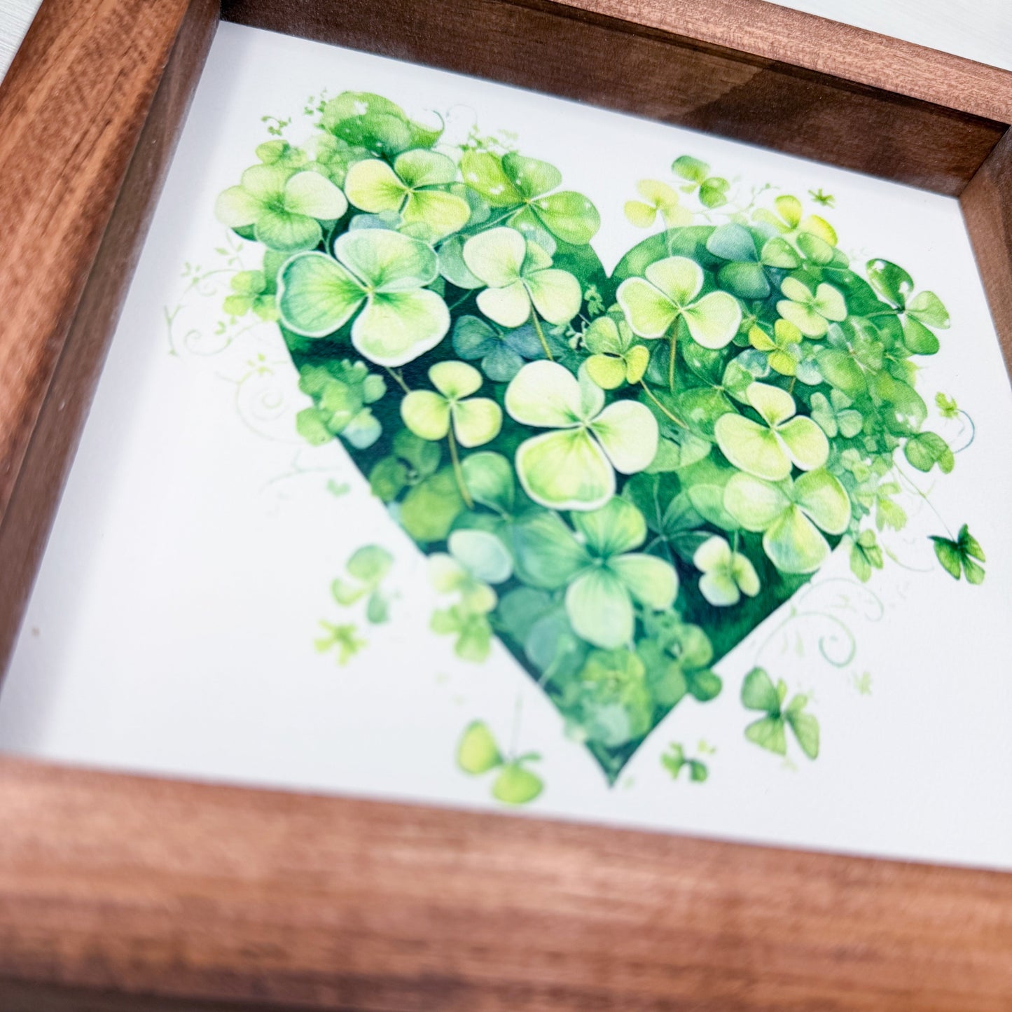 Framed artwork of a green heart-shaped plant design on white sign.
