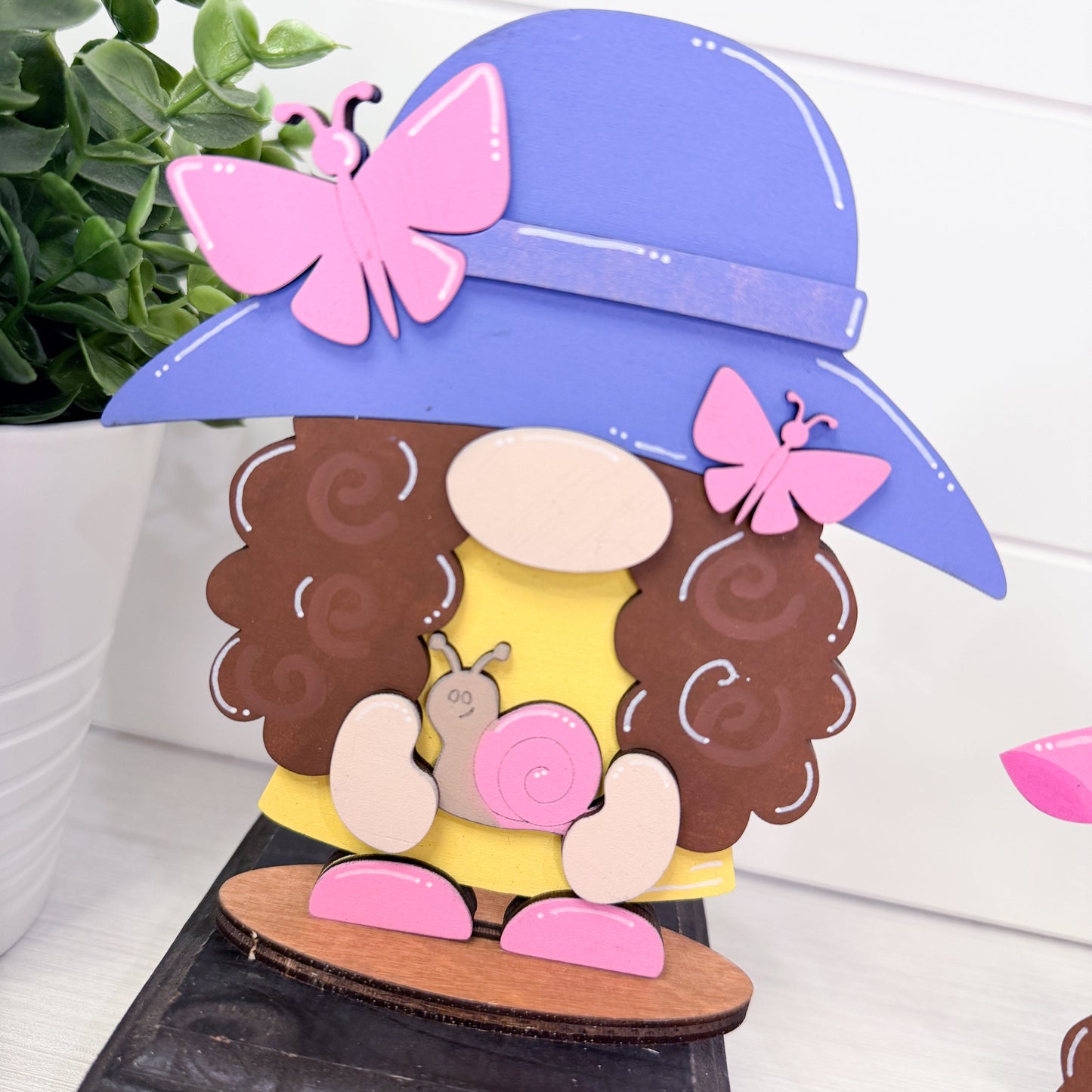 Decorative item with a character wearing a purple hat, brown hair, and pink butterfly, sitting on a wooden platform.