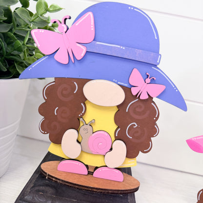 Decorative item with a character wearing a purple hat, brown hair, and pink butterfly, sitting on a wooden platform.