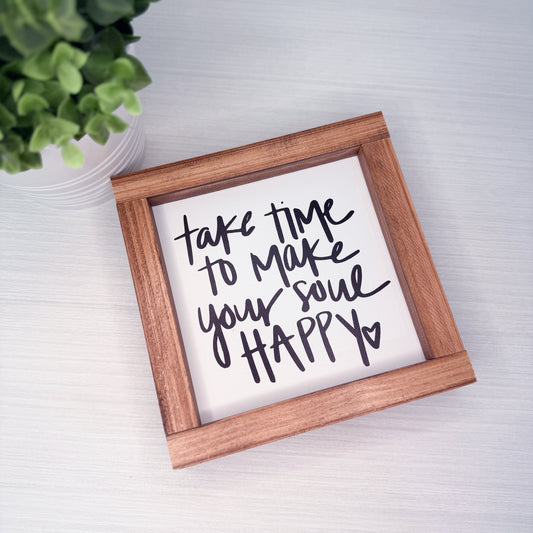 Wooden-framed sign with motivational quote on a light surface with a plant in the corner.