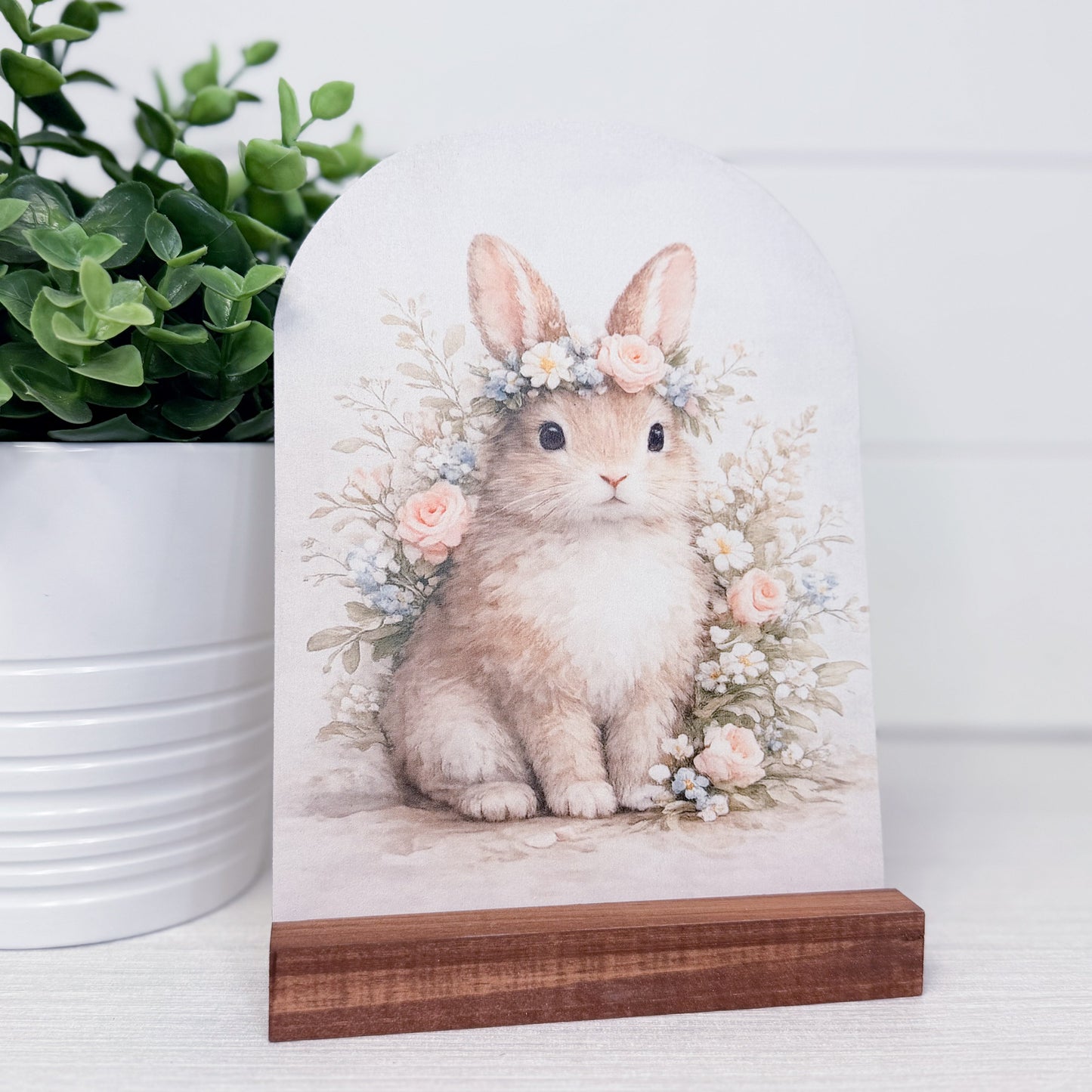 arch with a rabbit illustration wearing a floral crown on a wooden stand, with a plant in the background.