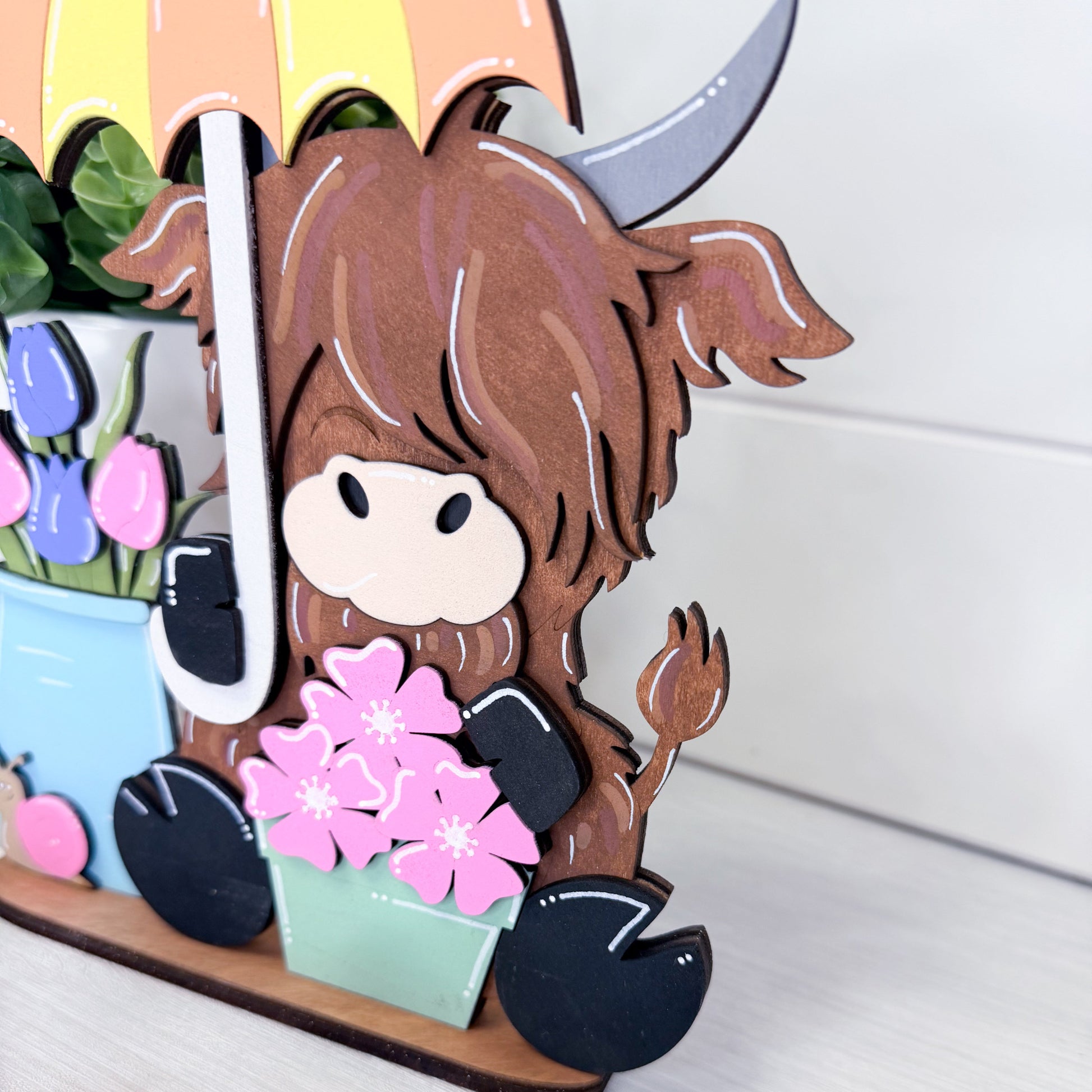 highland cow with brown hair and a colorful umbrella holding flowers.