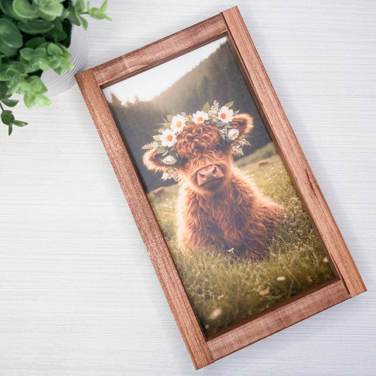 Framed picture of a fluffy animal with a flower crown on a white surface.